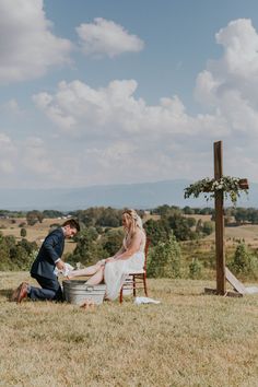 a bride and groom sitting on a chair in the grass with a cross behind them