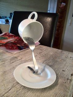 a spoon is pouring water into a white bowl on a wooden table with a black chair in the background