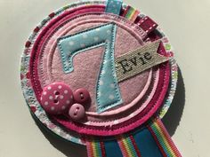 a pink and blue ribbon with a button on it next to a badge that says happy 7th birthday