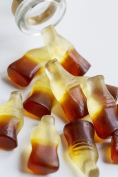 several pieces of gummy bears are being spilled into a glass jar on a white surface