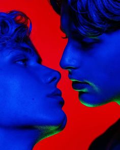 two young men are facing each other with blue and red lighting on their faces in front of them