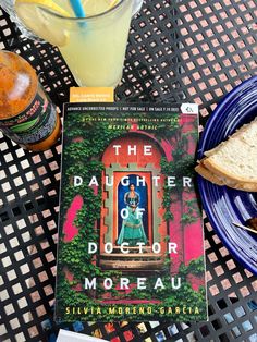 the daughter of doctor moreau sits on a table next to a drink and sandwich