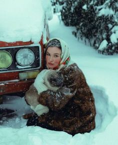 a woman sitting in the snow next to a car