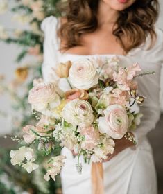 a woman holding a bouquet of flowers in her hands and wearing a white wedding dress