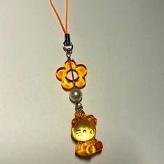 a yellow cat charm with a flower on it's end and a pearl bead in the middle