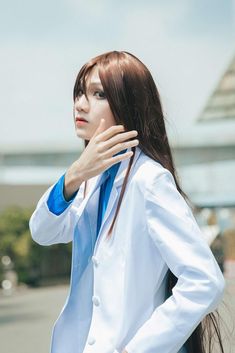 a woman with long brown hair wearing a white suit and blue shirt standing in front of a building