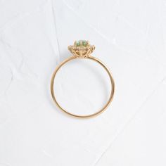 a gold ring with an emerald stone in the center on a white surface, top view