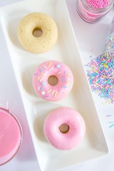 three doughnuts on a white plate with sprinkles and pink liquid