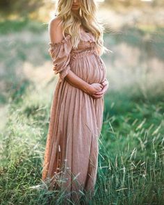 a pregnant woman standing in tall grass with her hands on her stomach wearing a pink dress