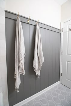 two white towels hanging on the wall next to each other in a bathroom with gray and white tiles