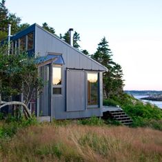 a small house sitting on top of a lush green hillside next to the ocean and trees