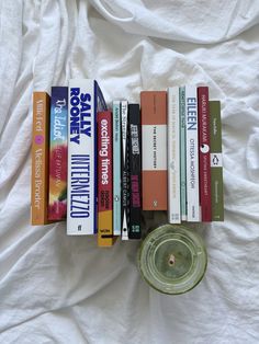 a stack of books sitting on top of a bed next to a glass jar filled with liquid