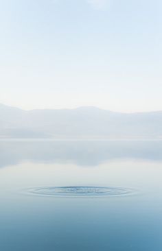 a large body of water sitting under a blue sky with mountains in the back ground