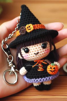 a small doll wearing a witches hat and holding a pumpkin keychain in her hand