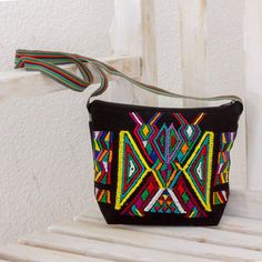 a small black bag with multicolored beading on the front and side, sitting on a wooden bench