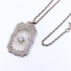 This stunning Art Deco pendant showcases the timeless beauty of camphor glass, set in intricate filigree work. The large center diamond accent in its buttercup setting adds a touch of luxury. Crafted by Esemco, a renowned jewelry maker founded in 1906 in Newark, NJ, this piece is a true collector's item. A 14k white gold chain completes the elegant ensemble. This piece exudes vintage style and sophistication. Perfect for Weddings, anniversaries, or other formal events or just add a a touch of ti Newark Nj, White Gold Chain, Art Deco Pendant, Filigree Pendant, Locket Charms, Jewelry Maker, Glass Set, Timeless Beauty, Pendant Necklaces