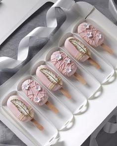 four pink and white decorated ice creams in a box with ribbons on the side