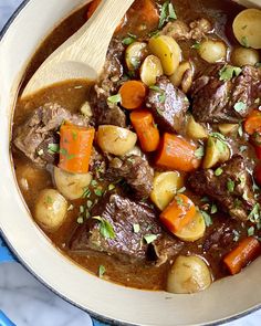 a pot filled with stew and carrots on top of a blue stovetop next to a wooden spoon