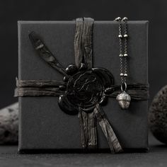 a gift wrapped in black paper and tied up with a silver chain, sits next to some rocks