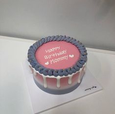 a pink and blue birthday cake with white icing on it's top, sitting on a table