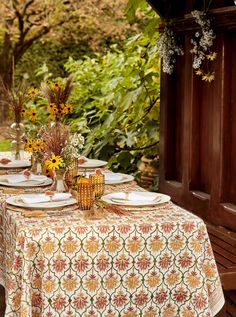 an outdoor table set with plates and flowers