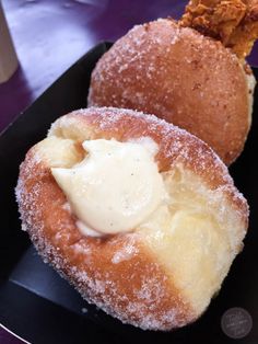 two donuts covered in powdered sugar sit on a black plate next to a cup of coffee