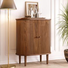 a wooden cabinet sitting next to a lamp on top of a hard wood floor near a potted plant