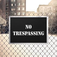 a no trespassing sign on a chain link fence in front of some buildings