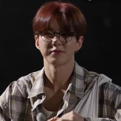 a woman with red hair and glasses sitting in front of a black background, looking at the camera