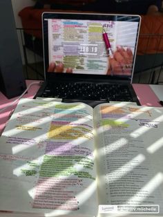 an open book sitting in front of a laptop on top of a pink tablecloth