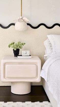 a white nightstand with a plant on it next to a bed