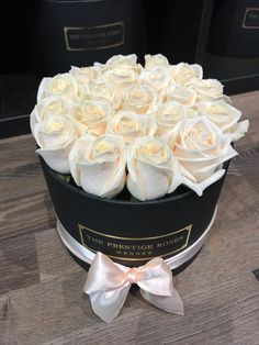 white roses in a black box with a bow on the top, sitting on a wooden table