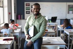 a man sitting on top of a desk in a classroom