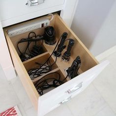 an open drawer with many cords and remotes in it on the floor next to a wall