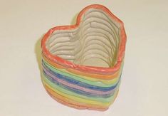 a rainbow heart shaped bowl on a white table with the lid open and stacked in it