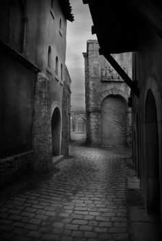 black and white photograph of cobblestone street in an old european town with arched doorways