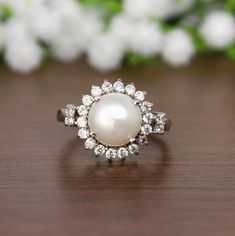 a pearl and diamond ring sitting on top of a wooden table next to white flowers