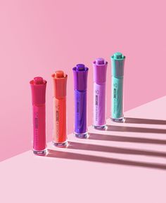 five different colored tubes are lined up on a pink and blue surface with shadows from them