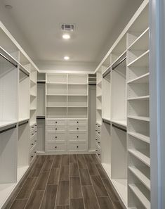 an empty walk - in closet with white shelving and wood flooring on the walls