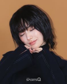 a woman with black hair and bangs wearing a black jacket looking down at her hand