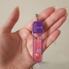 a hand holding a purple and pink toothbrush shaped keychain in it's palm