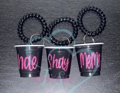 three black plastic cups with pink lettering on them and two rubber rings hanging from each one