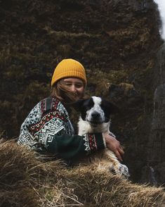 a woman holding a dog on top of a grass covered hillside next to a waterfall