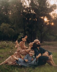 three people are laying on the grass in front of trees and one person is holding a flower