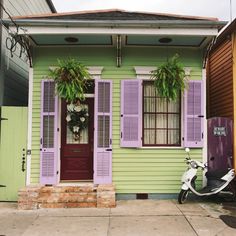 a scooter parked in front of a green house with purple shutters and potted plants