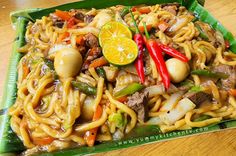 a green tray filled with noodles, meat and veggies on top of a wooden table