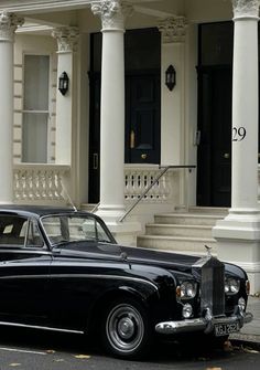 an old black car parked in front of a white building with pillars and columns on the sides