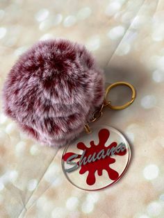 a furry ball keychain sitting on top of a white sheet with red letters