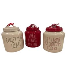 three ceramic kitchen canisters with christmas treats written on the front and bottom, one red