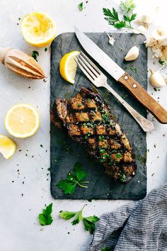 a piece of meat on a cutting board with lemons, garlic and parsley